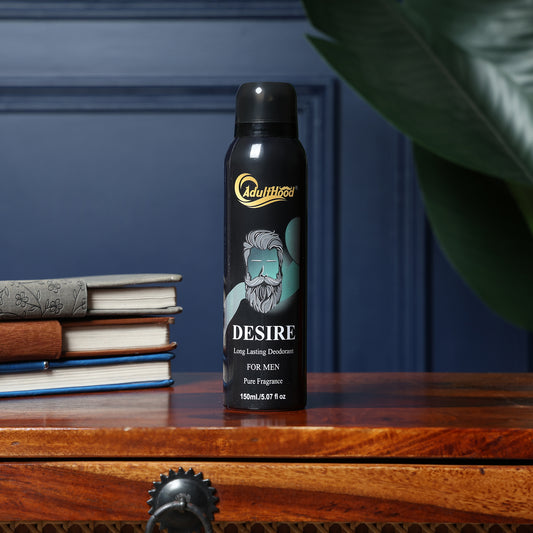 Adultiqo Desire deodorant spray bottle on a wooden surface with books and a plant in the background.