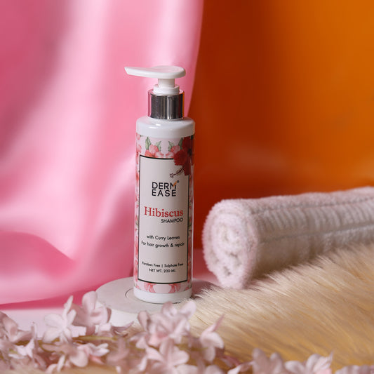 Derm Ease Hibiscus shampoo bottle with flowers and towel on a blurred background